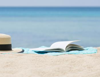 hat and open book on sandy beach